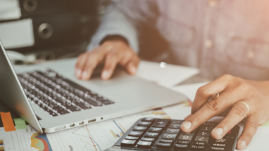 Person with a laptop and caluculator preparing a financial report